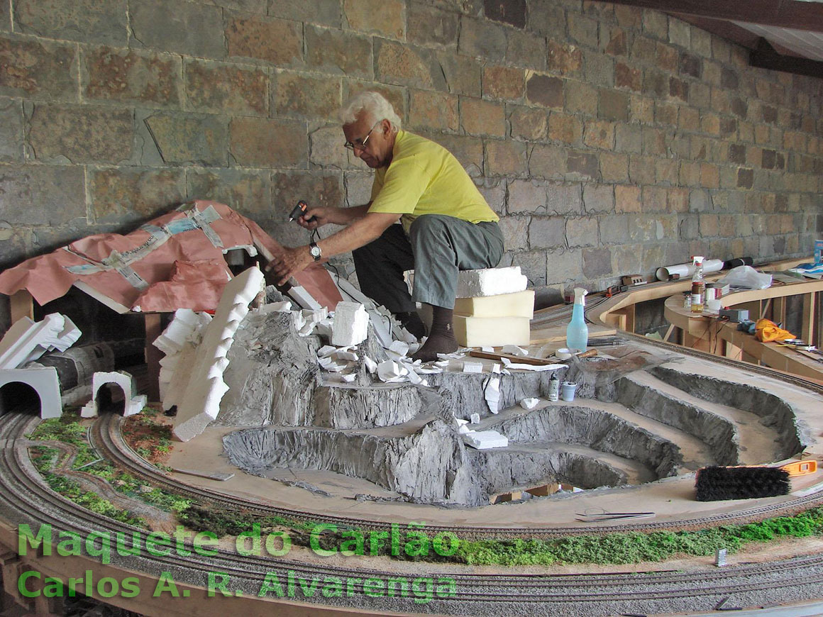 Um suporte de madeira, pedaços de isopor e papel de jornal formam o corpo da montanha na maquete de ferreomodelismo