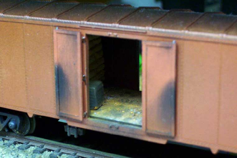 Ferreomodelo de vagão com as portas avertas, vendo-se o piso e a imitação de carga em miniatura